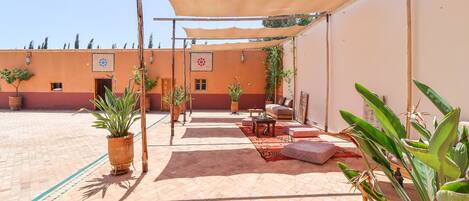 A courtyard with a shaded seating area, potted plants, and a tiled floor.