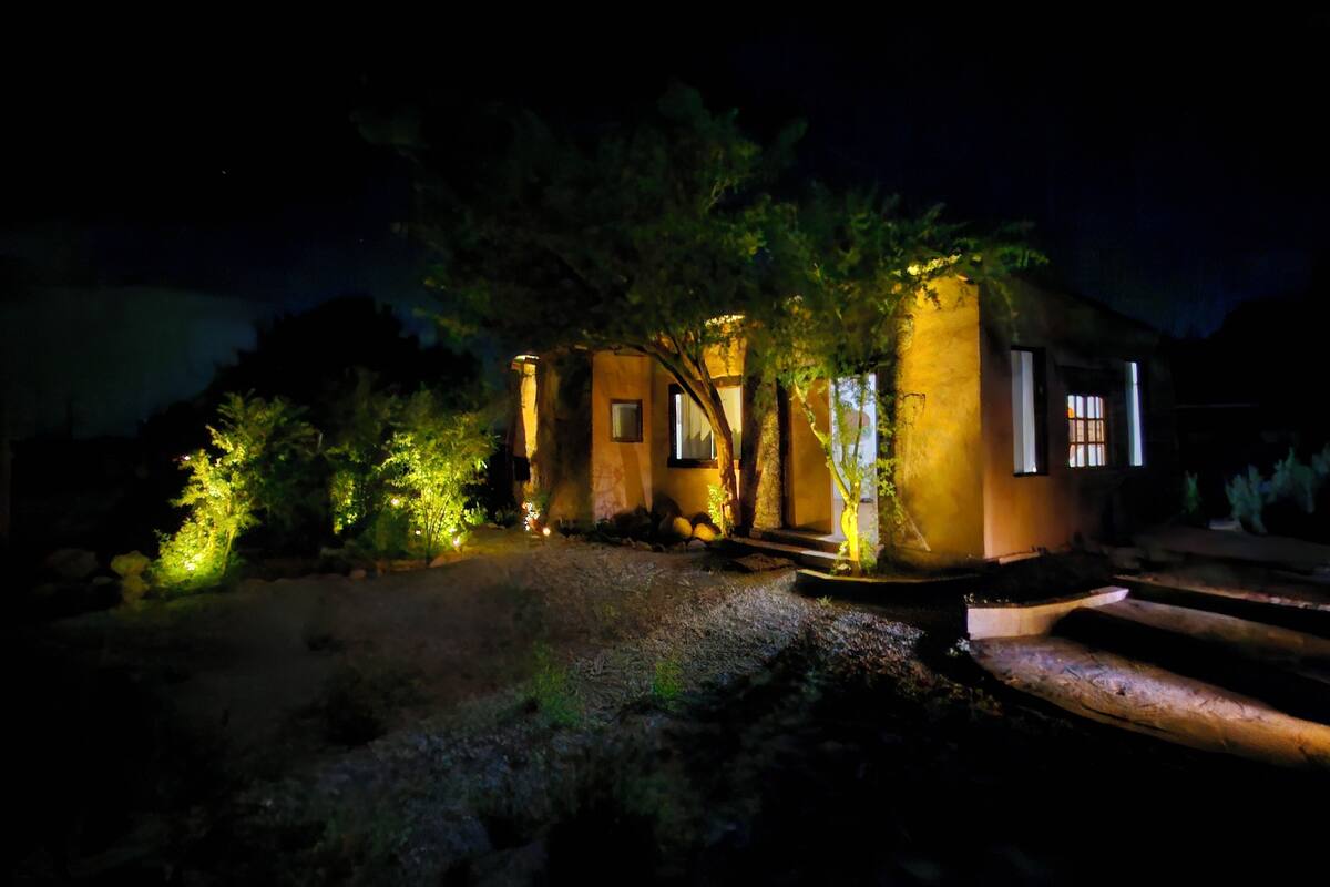 A small, single-story building with a warm exterior, illuminated windows, and a gravel pathway leading to the entrance.