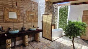 Un baño con baldosas de piedra, un banco de madera y una pequeña planta.