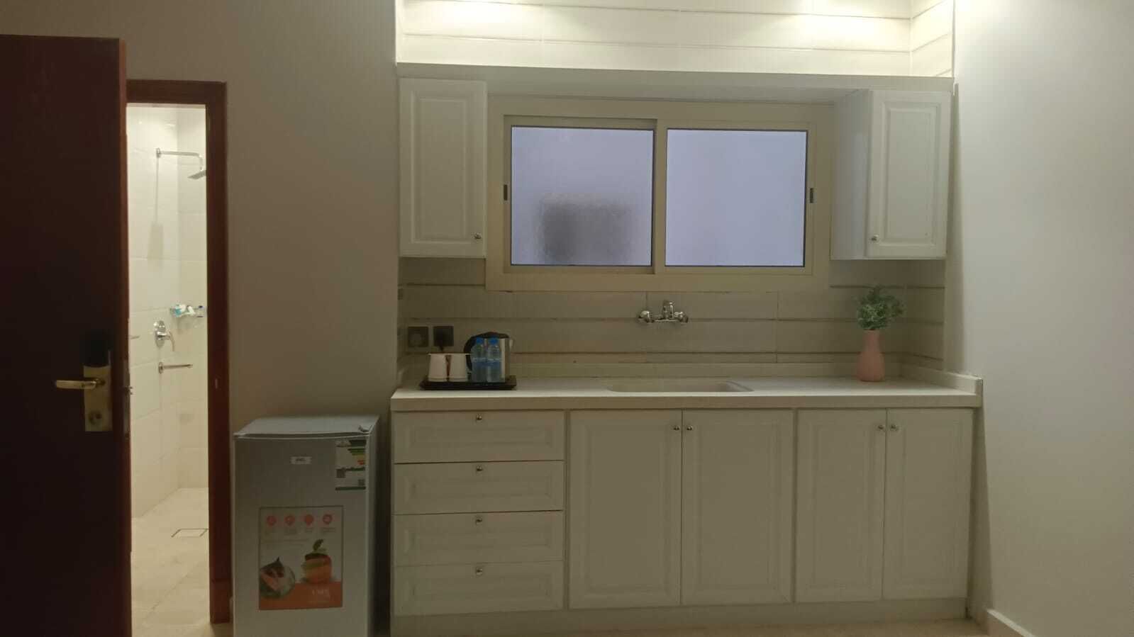 A small kitchen with white cabinets, a double sink, and a refrigerator.