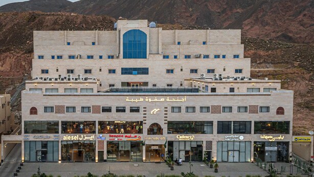 A multi-story hotel with a central atrium, retail shops on the ground floor, and a mountainous backdrop.