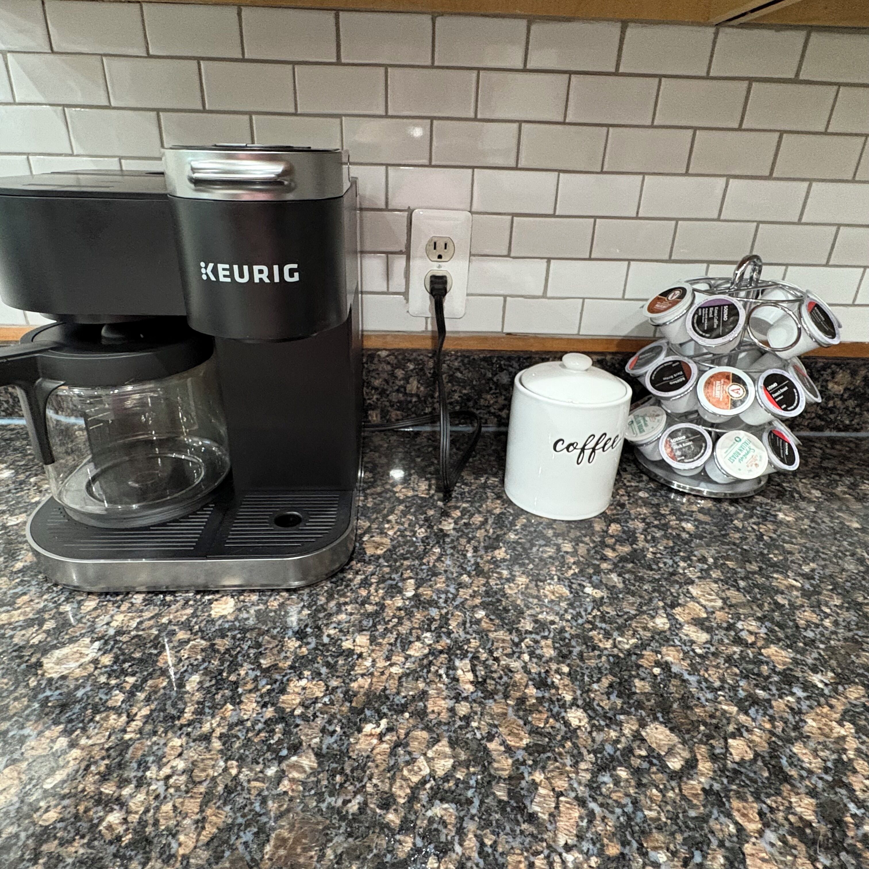 Eine Kaffeemaschine von Keurig auf einer Granit-Arbeitsplatte, mit einer Kaffeetasse und einem Tablett für mehrere Kaffeekapseln.