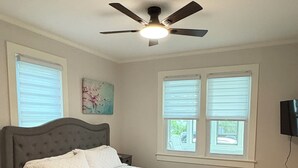 A bedroom with a bed, a ceiling fan, and two windows with blinds.
