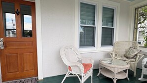 A porch with a wooden door, two wicker chairs, a round table, and a ceiling fan.
