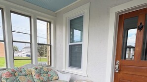 A porch with a floral sofa, a small round table, and a wooden door with a welcome mat.