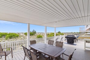 A covered outdoor patio with a table and chairs, a grill, and a view of the landscape.