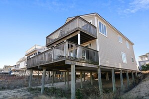 Een tweelaags huis met een balkon op de eerste verdieping, gebouwd op houten palen aan een zandstrand.