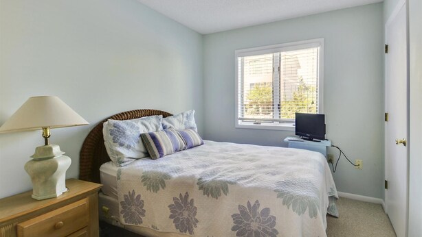 A bedroom with a bed, a nightstand, a lamp, a television, and a window with blinds. - OceanFront 8 Bedroom! (South Bethany)