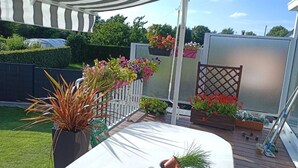 Un patio con una mesa blanca, plantas en macetas y cestas colgantes de flores.
