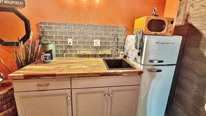 Una cocina compacta con encimera de madera, un fregadero, un refrigerador antiguo y un salpicadero de ladrillo.