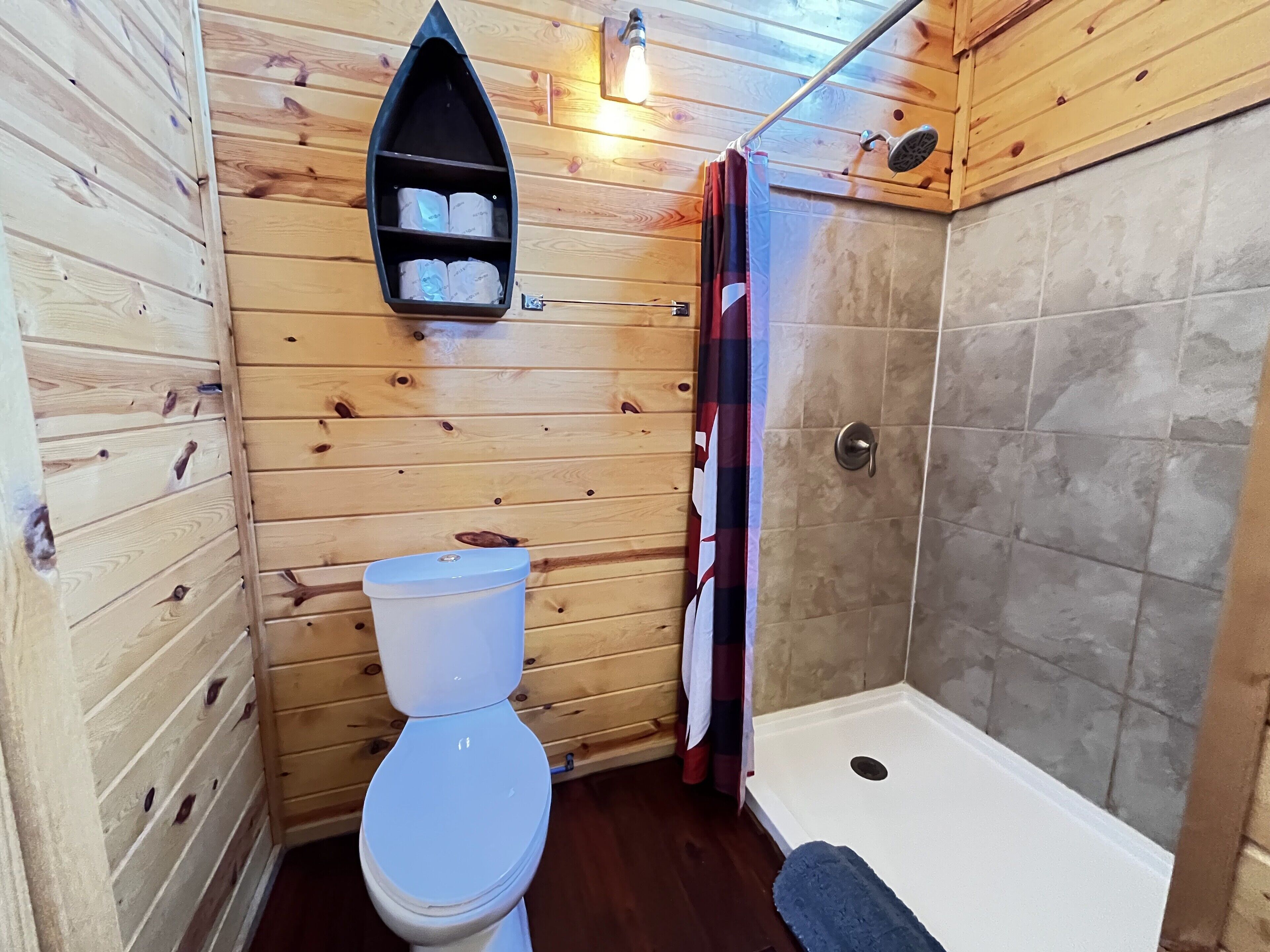 A wooden cabin bathroom with a toilet, a shelf with toiletries, and a shower area.