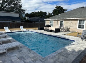 Une piscine rectangulaire avec une terrasse carrelée, entourée de chaises longues et d’un espace barbecue.