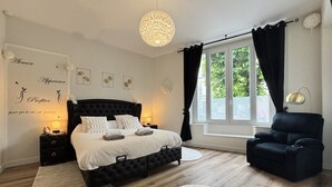 A bedroom with a large bed, a side table, a chair, a window with curtains, and a wall with decorative text. - Apartment 1. Attractive apartment (t2 of 60m2) on air-conditioned ground floor with terrace. (Limoges)