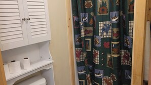 Un baño con inodoro, un armario con papel higiénico y una cortina de ducha a cuadros.