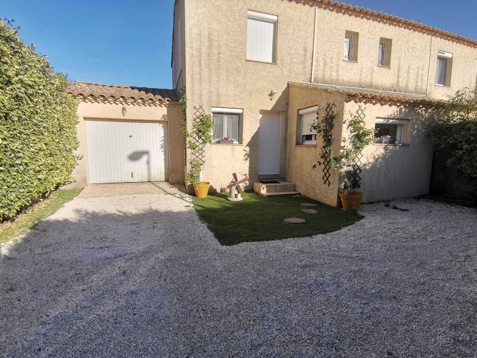 En tvåvåningsbyggnad med en vit garageport, en liten framträdgård med gräsmatta och krukväxter samt en grusuppfart.