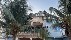 A two-story building with a light blue facade, a stone accent wall, and a balcony with a view. - Luxury 2BR Accra, Near Beach with WiFi, Breakfast, 20min Airport. (Gbawe)