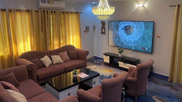 A modern living room with a brown sofa, a glass coffee table, and a chandelier. - Luxury 2BR Accra, Near Beach with WiFi, Breakfast, 20min Airport. (Gbawe)