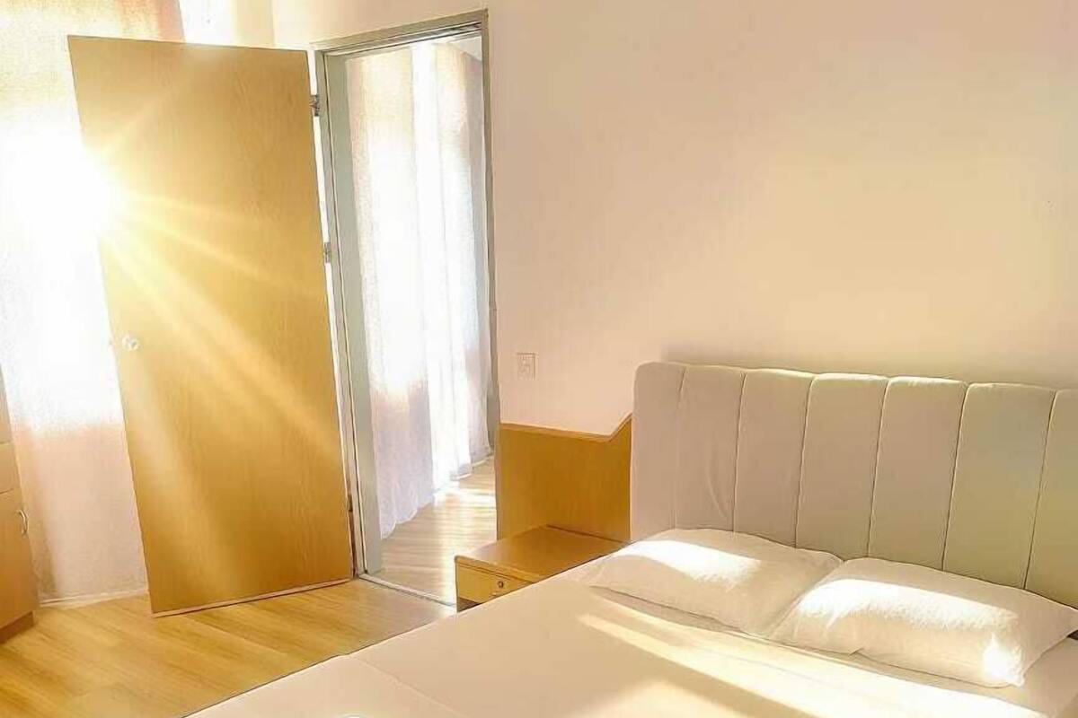 A modern hotel room with a large bed, a wooden floor, a mirror, and a door with curtains.