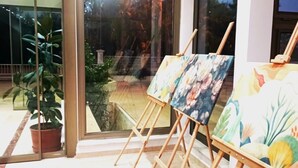 A modern interior with large windows, wooden easels with paintings, and a potted plant. - Softa Vivanco Hotel (Bozyazi)