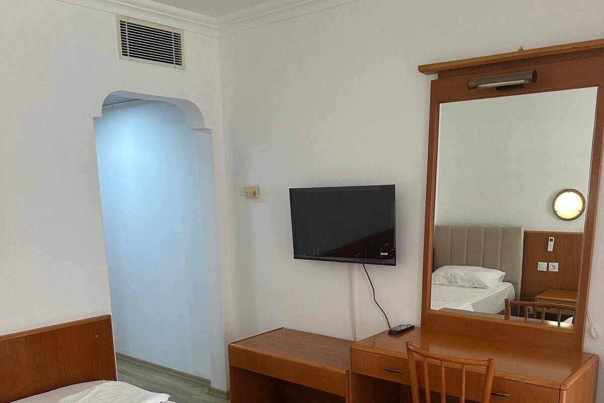 A hotel room with two single beds, a wooden desk with a chair, a television, and a mirror.