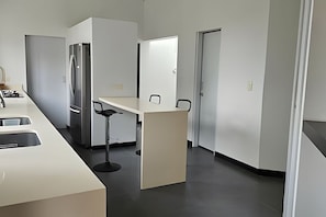 Een moderne keuken met een roestvrijstalen koelkast, een wit aanrecht en een barkruk.