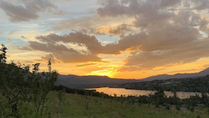 Un paisaje con atardecer sobre una masa de agua, rodeado de colinas y vegetación.