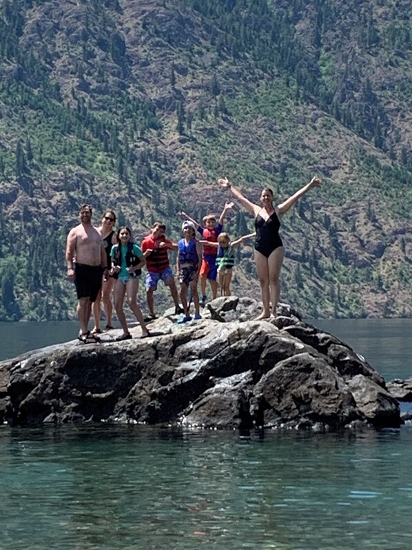 A group of people standing on a rocky outcrop by a body of water with a mountainous backdrop.