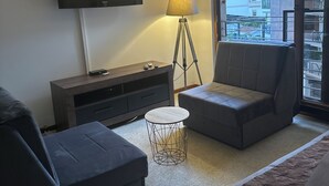 A modern hotel room with a large window, a flat-screen TV, a lamp, and a sofa. - Mik Apartments Heart of Budva 1+1 40sqm (Budva)