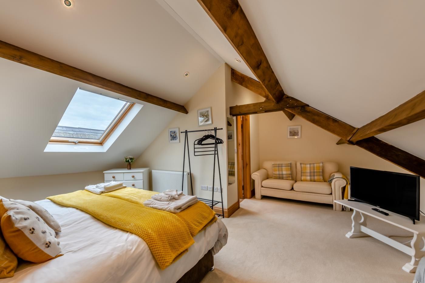 A bedroom with a bed, a TV, a sofa, a radiator, and a window.