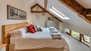 Een slaapkamer met een schuine plafond, een bed met wit beddengoed, een rood kussen, een dressoir en een schilderij aan de muur.