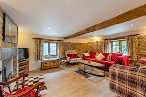 A cozy living room with a stone wall, a fireplace, a red sofa, and a wooden coffee table.