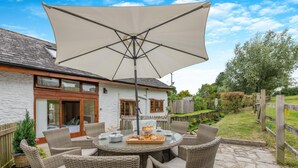 Een terras met wicker meubels, een ronde tafel en een grote parasol.