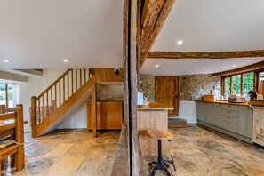 A rustic kitchen with a wooden staircase, stone walls, and a stone floor.