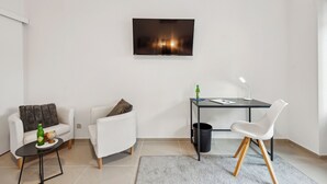 A modern living room with a white sofa, a white armchair, a small table with a bottle and a globe, a desk with a chair, and a flat-screen TV mounted on the wall. - Central location... Ideal for business people, fitters...3 rooms, WiFi, SmartTVs (Mettmann)