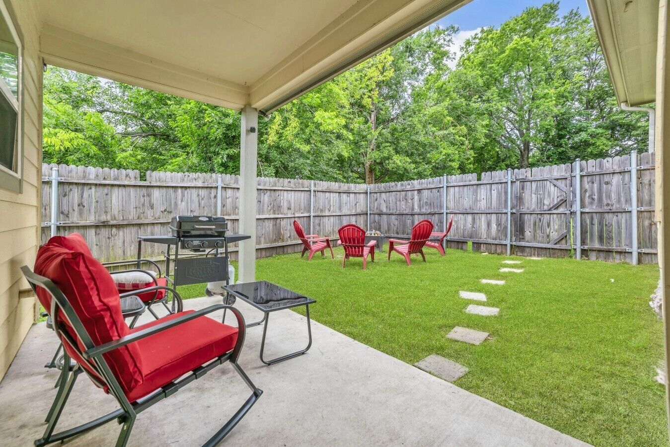 Eine überdachte Terrasse mit Grill, roten Stühlen und einem Betonboden.