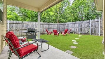 Eine überdachte Terrasse mit Grill, roten Stühlen und einem Betonboden.