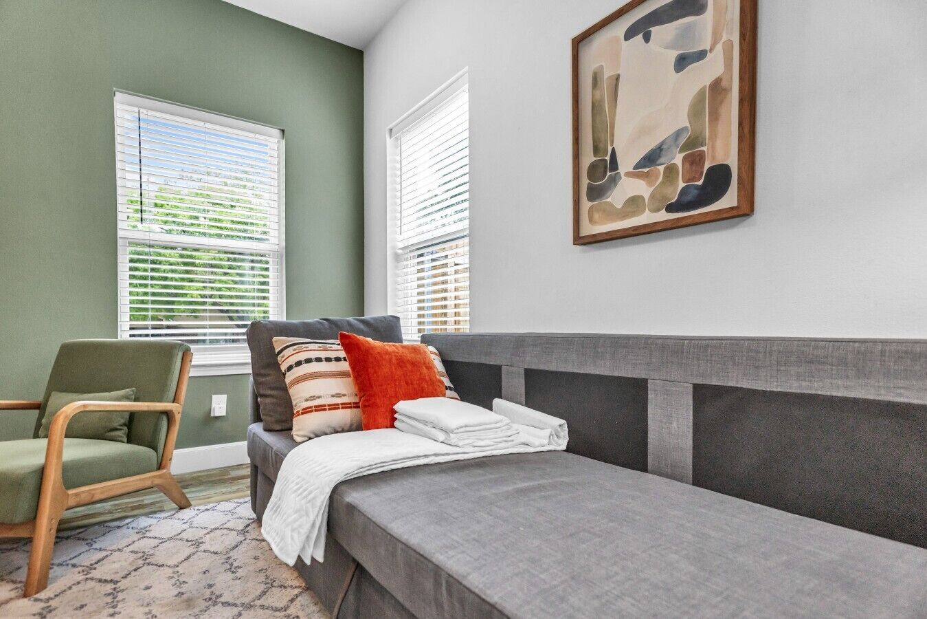 A room with a bed, a chair, and a painting on the wall.