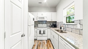 A modern kitchen with white cabinets, a granite countertop, and a built-in oven. - Historic DT, Private, 30 Min to Dal | TSA (Rockwall)