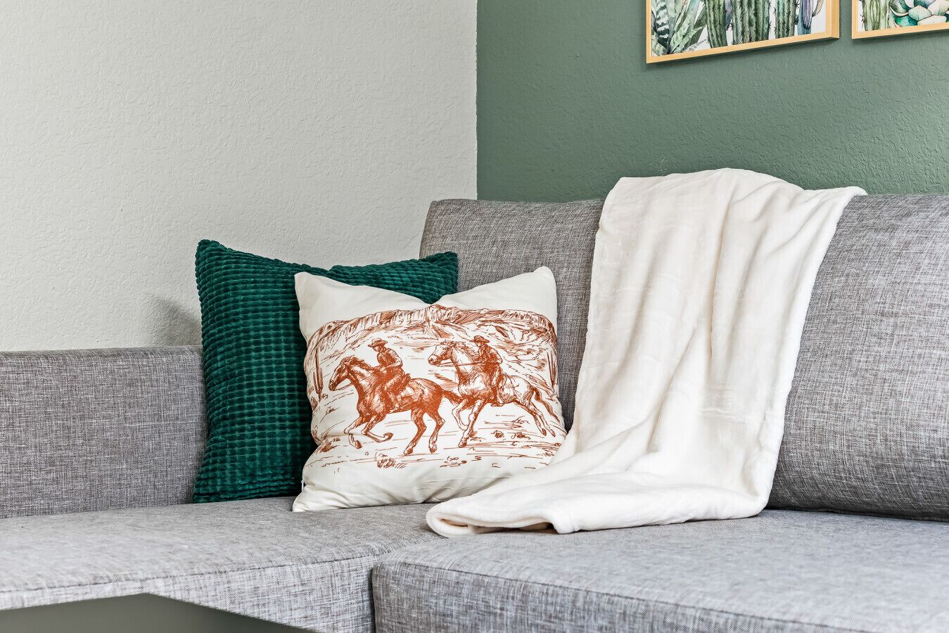 A grey sofa with a white throw blanket and two decorative pillows, one green and one with a horse print.