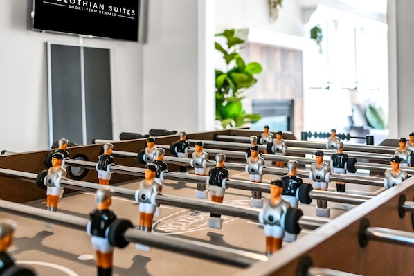 A foosball table in a hotel lobby with a television above it and a plant in the background.