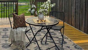 A patio with a round table, two chairs, a vase with flowers, and string lights. - Creston Centennial #1-King bed, rustic barn loft w/stairs (Kalispell)