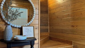A wooden interior with a round mirror, a vase with branches, and a framed quote on a black console table. - Creston Centennial #1-King bed, rustic barn loft w/stairs (Kalispell)