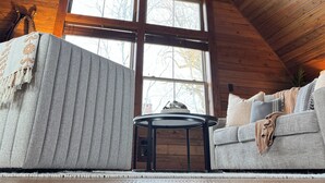 A cozy cabin interior with wooden beams, a ceiling fan, a sofa, and a table. - Creston Centennial #1-King bed, rustic barn loft w/stairs (Kalispell)