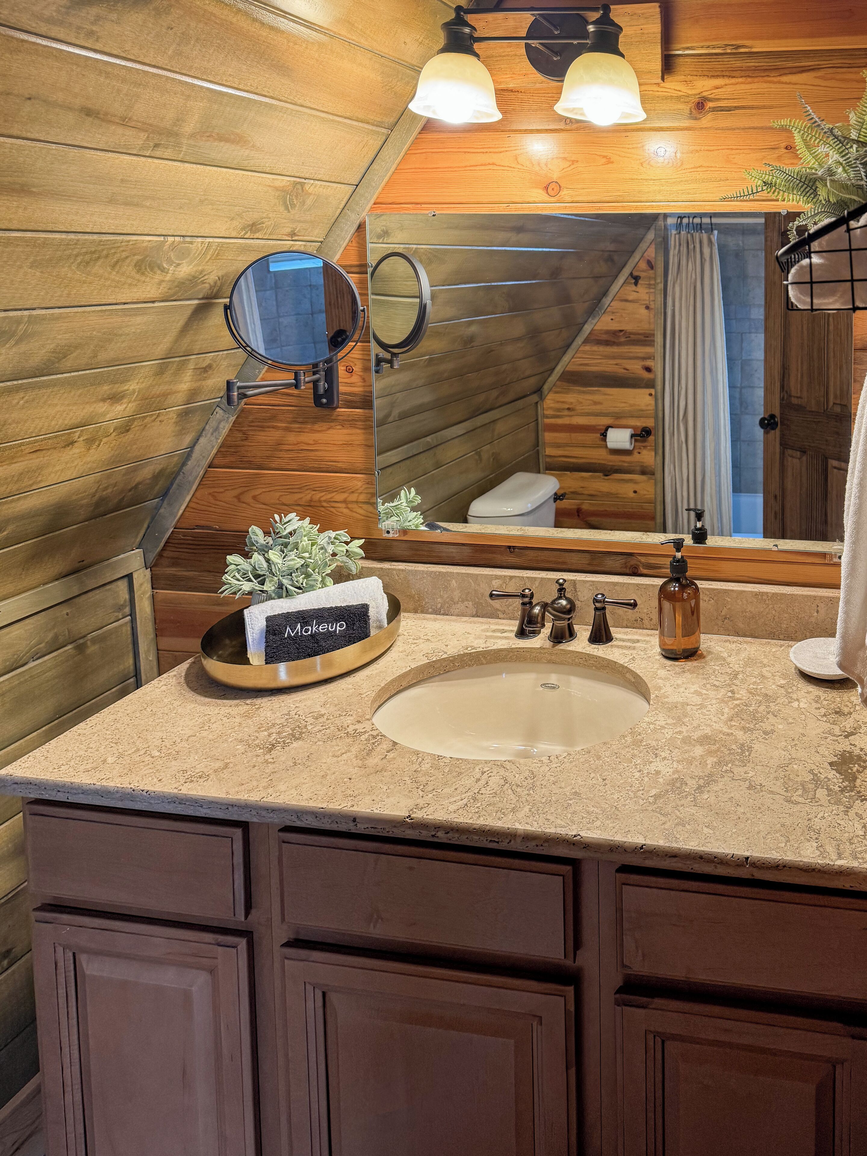 A bathroom with wooden walls, a large mirror, a sink with a basin, a makeup tray, and a towel rack.