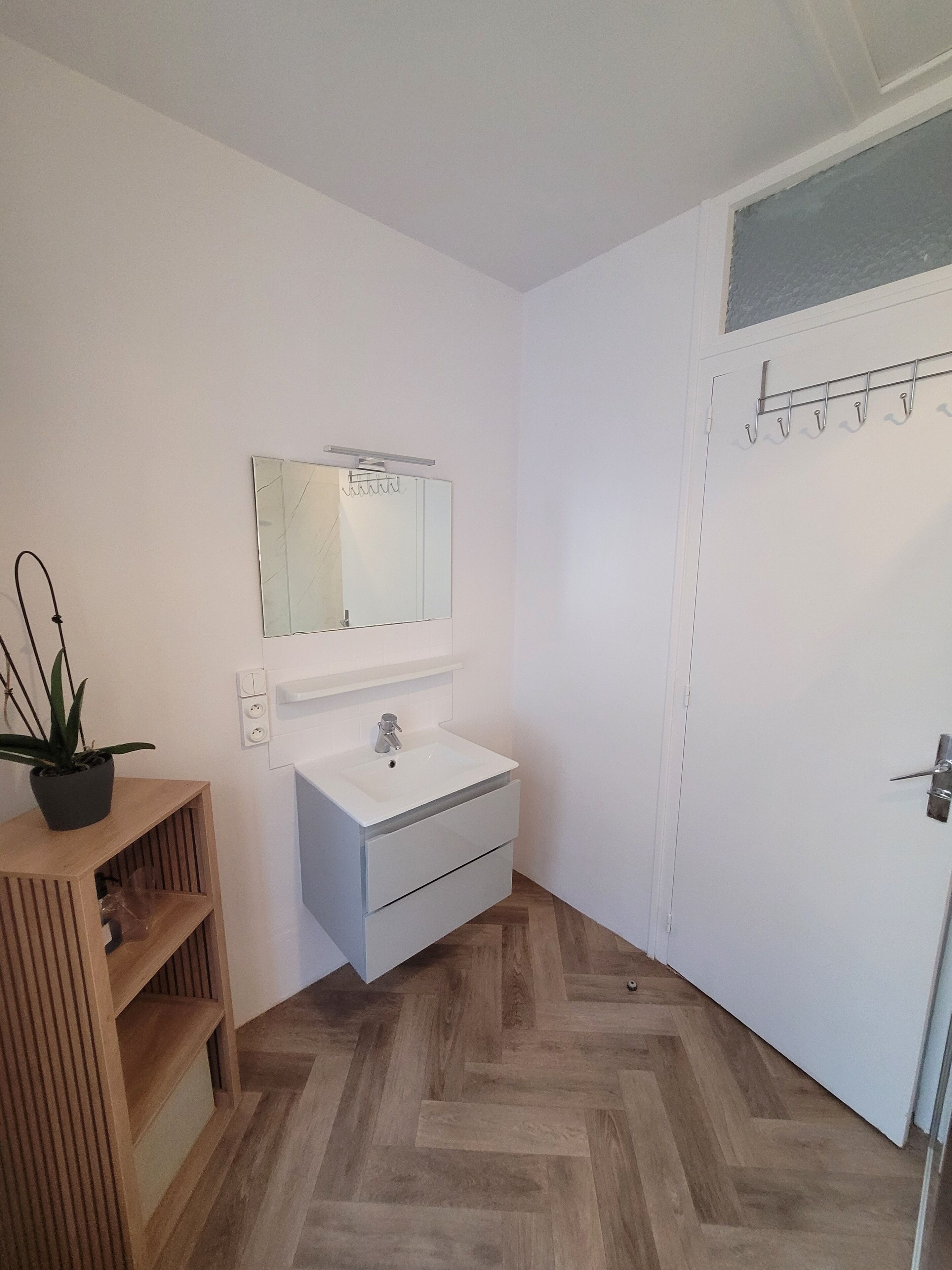 Ein kleines, sauberes Badezimmer mit Waschbecken, Spiegel und Holzboden.