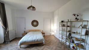Ett sovrum med en säng, ett sängbord, en hängande lampa, en spegel och en hylla med olika föremål.