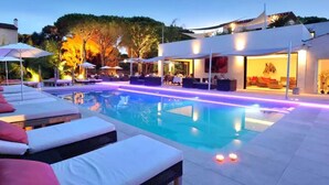 A swimming pool with lounge chairs and umbrellas, a covered seating area, and a building with a modern design. - Air-conditioned 35m² apt, private garden, pool, parking, Wi-Fi, near sea (cogolin)