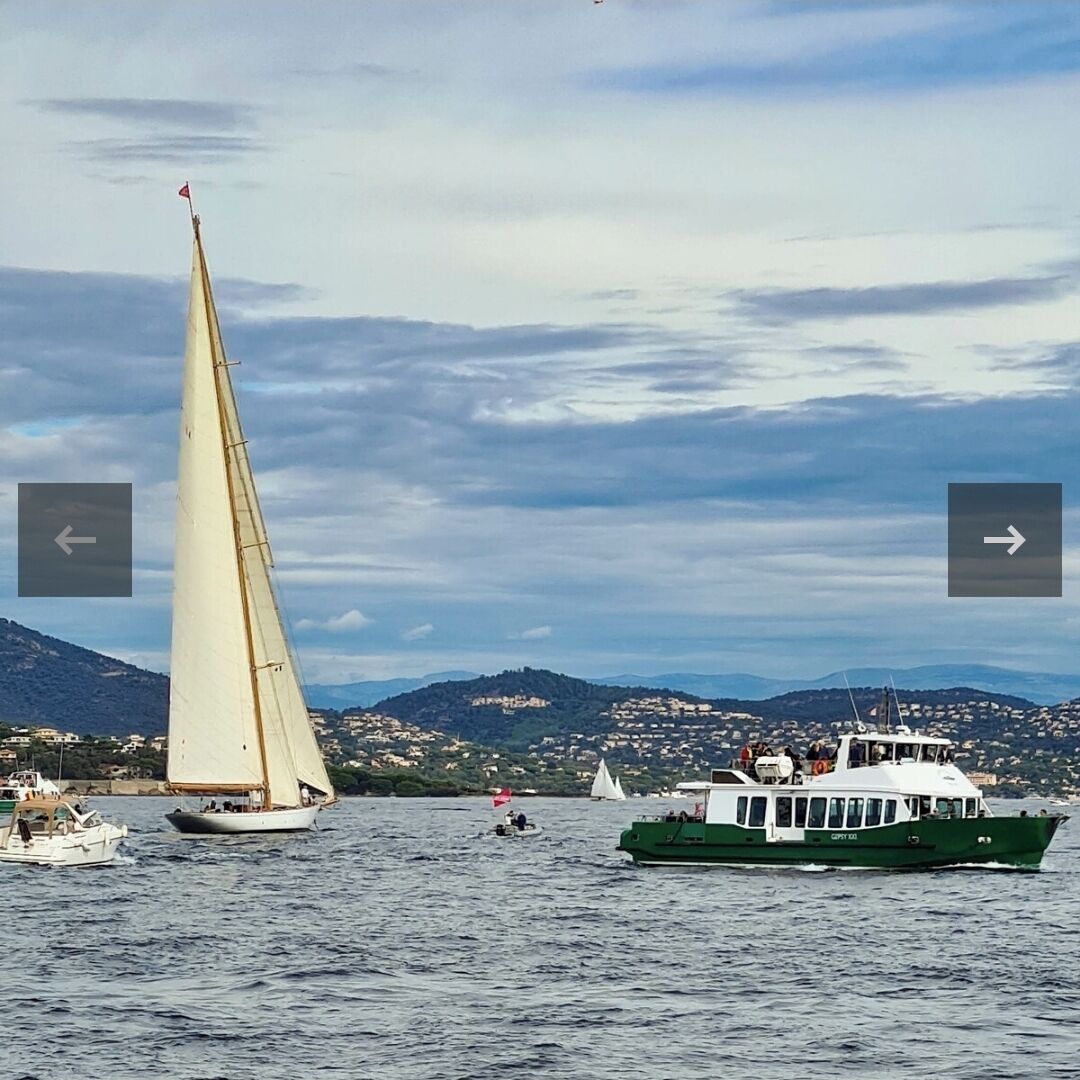 A sailboat with a white sail and a green boat with a white cabin in the water.