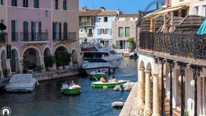 A canal with boats, buildings with balconies, and a covered walkway. - Air-conditioned 35m² apt, private garden, pool, parking, Wi-Fi, near sea (cogolin)
