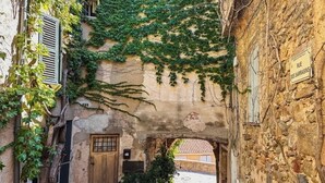 A narrow stone alleyway with a rustic stone building on the right, a wooden door, and a sign reading "Rue des Sarrasins". - Air-conditioned 35m² apt, private garden, pool, parking, Wi-Fi, near sea (cogolin)